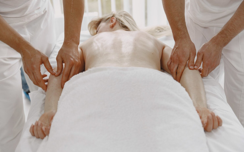 Two licensed massage therapists at Uniq Massage in McKinney TX performing a synchronized four hands massage on a relaxed guest